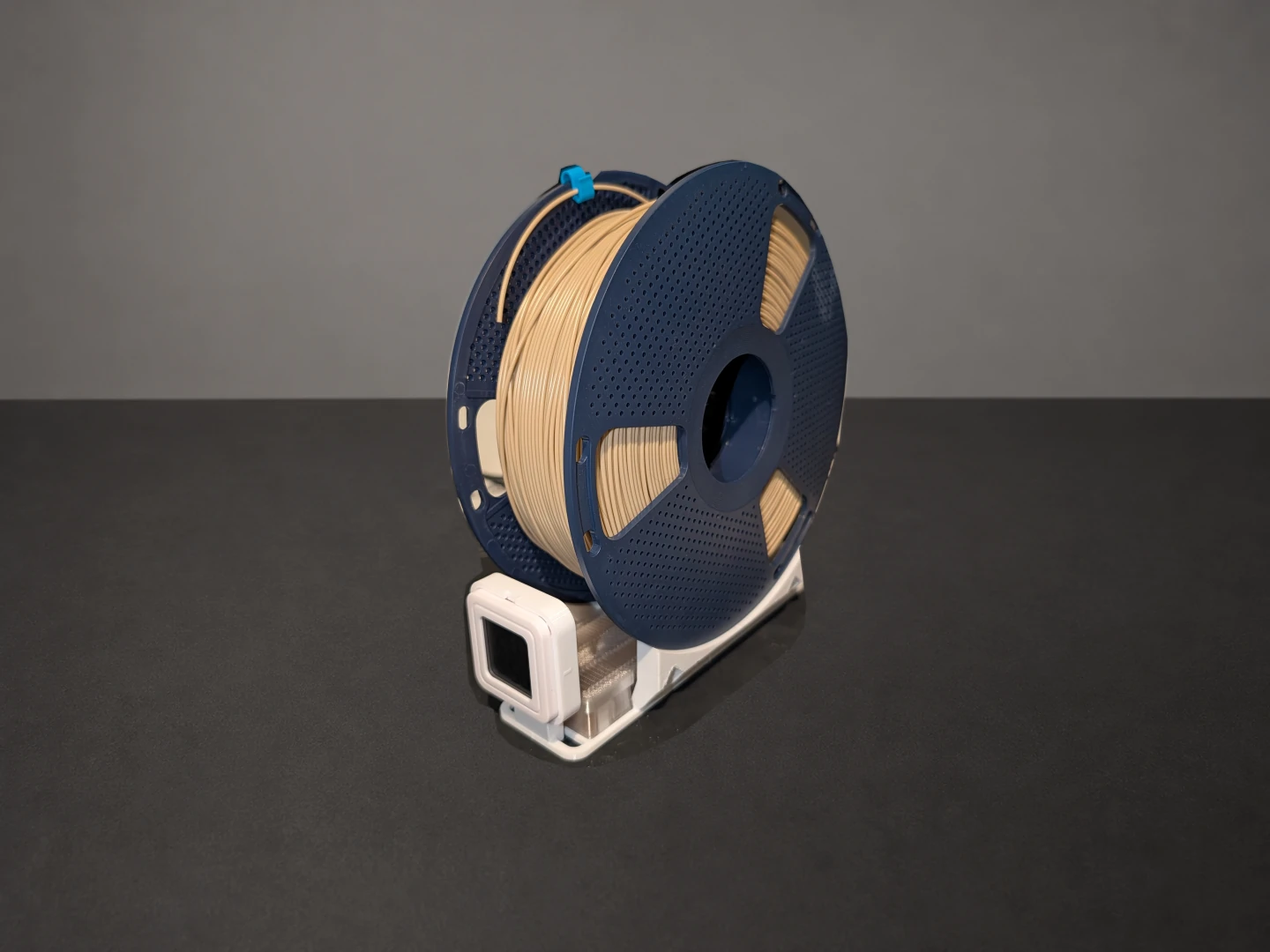 Filament spool standing on a white printed cradle, with a square meter at the front and translucent tray underneath.